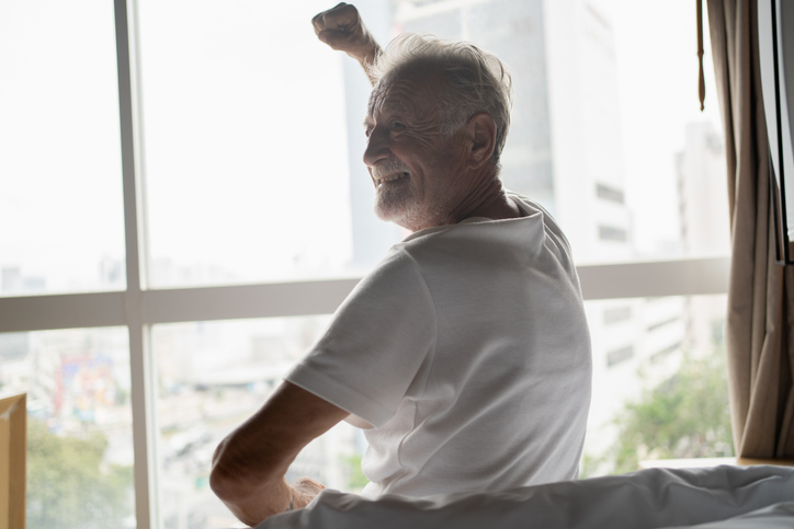 male sitting in front of window with arm raised and smiling in personal residence