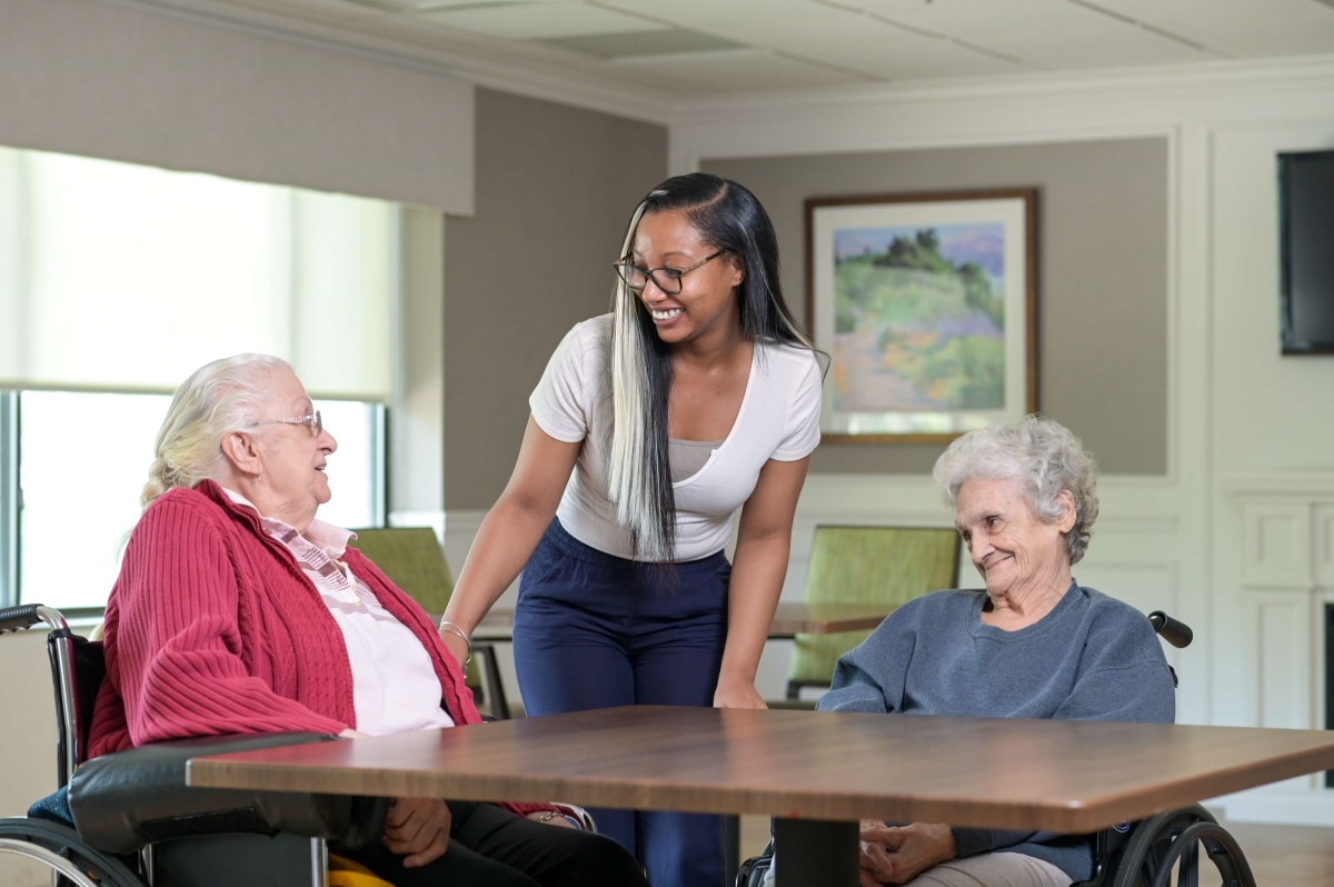 two older adult ladies at a table talking with female colleague greeting them standing up