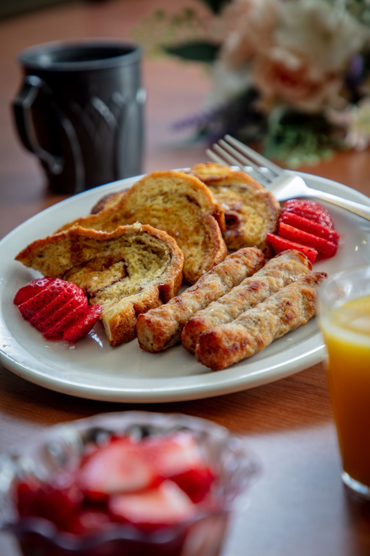 Breakfast image of French toast, sausage, fruit and juice