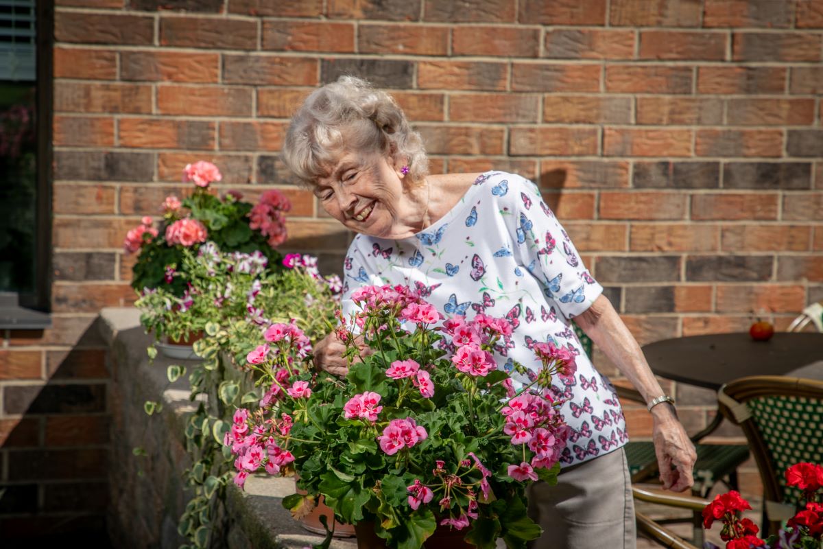 older adult female enjoying pink flowers on the patio at St. Paul's