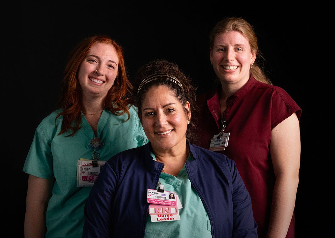 Three smiling nurses from the Burdett Birth Center at Samaritan Hospital pose together against a dramatic black background.