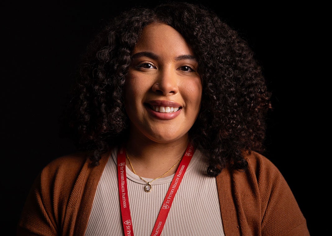 Dramatic close-up of a mammography staffer - the young, black professional woman smiles against a dark background.