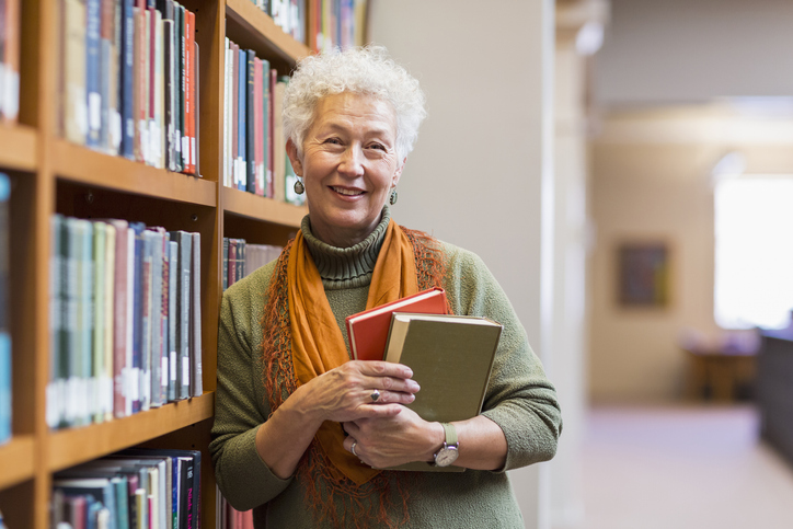 older female holding books in library